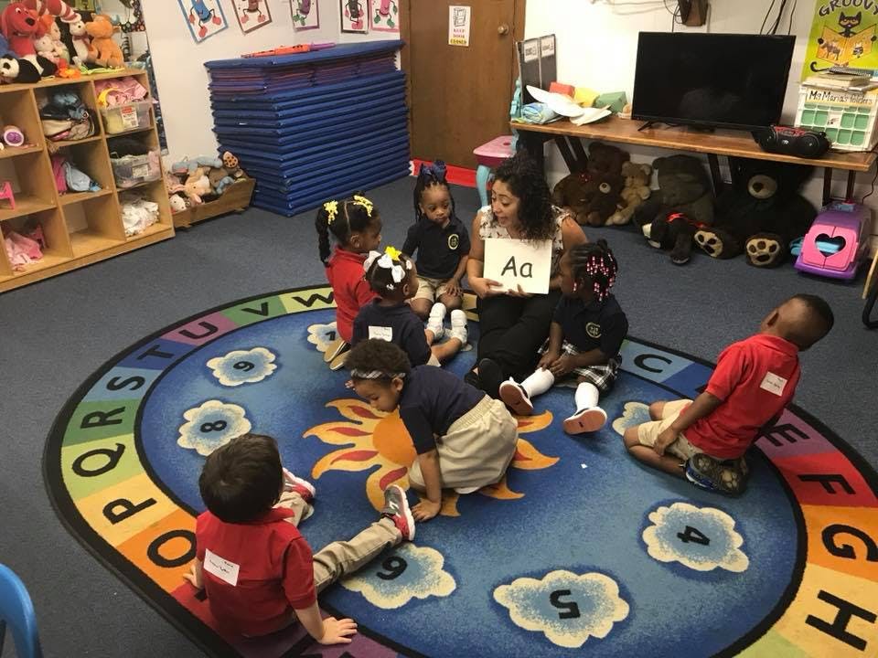Adult holding up a letter A card to children sitting on a rug