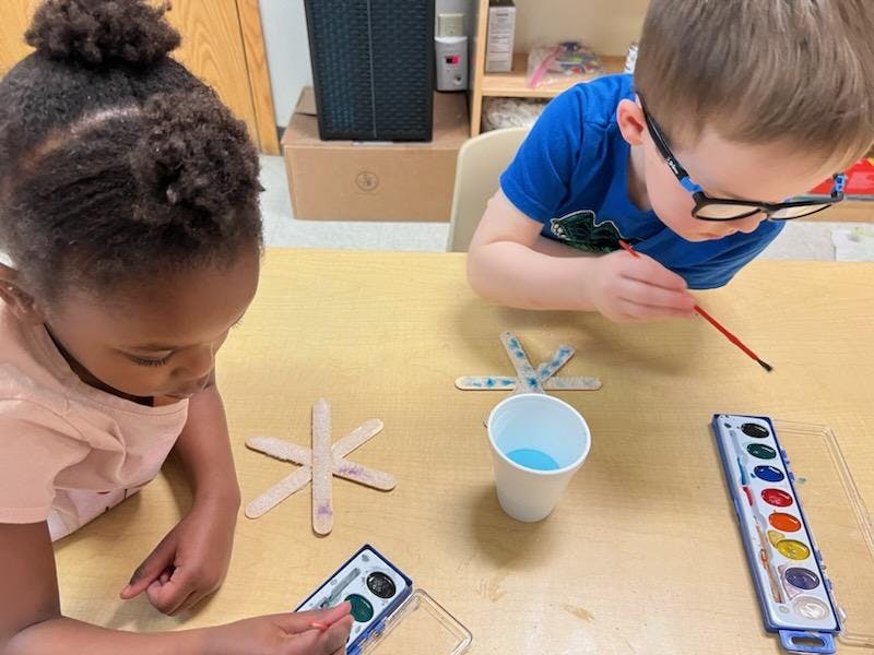 Two children painting craft sticks at a table