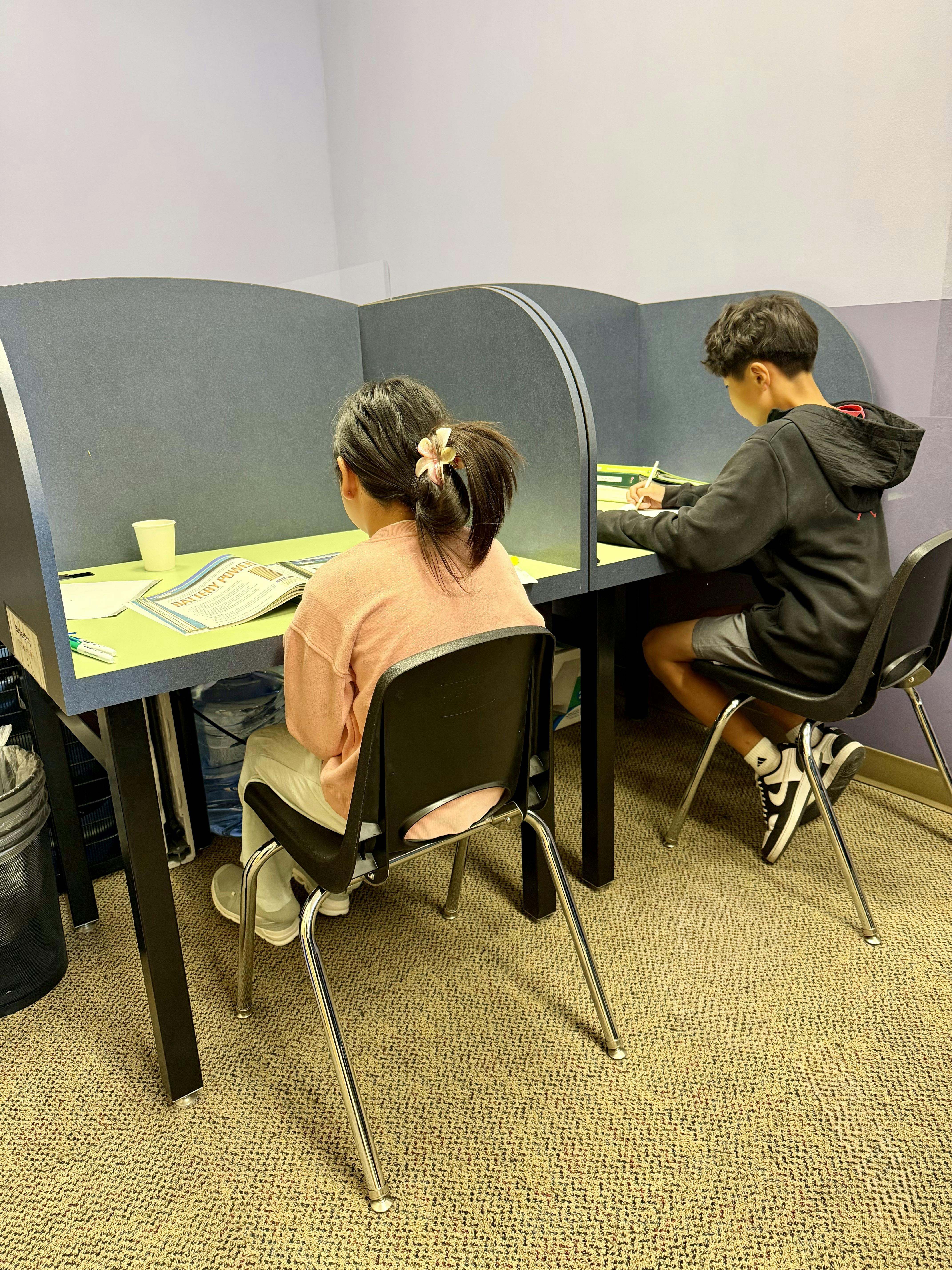 Two children sitting in study carrels reading and writing