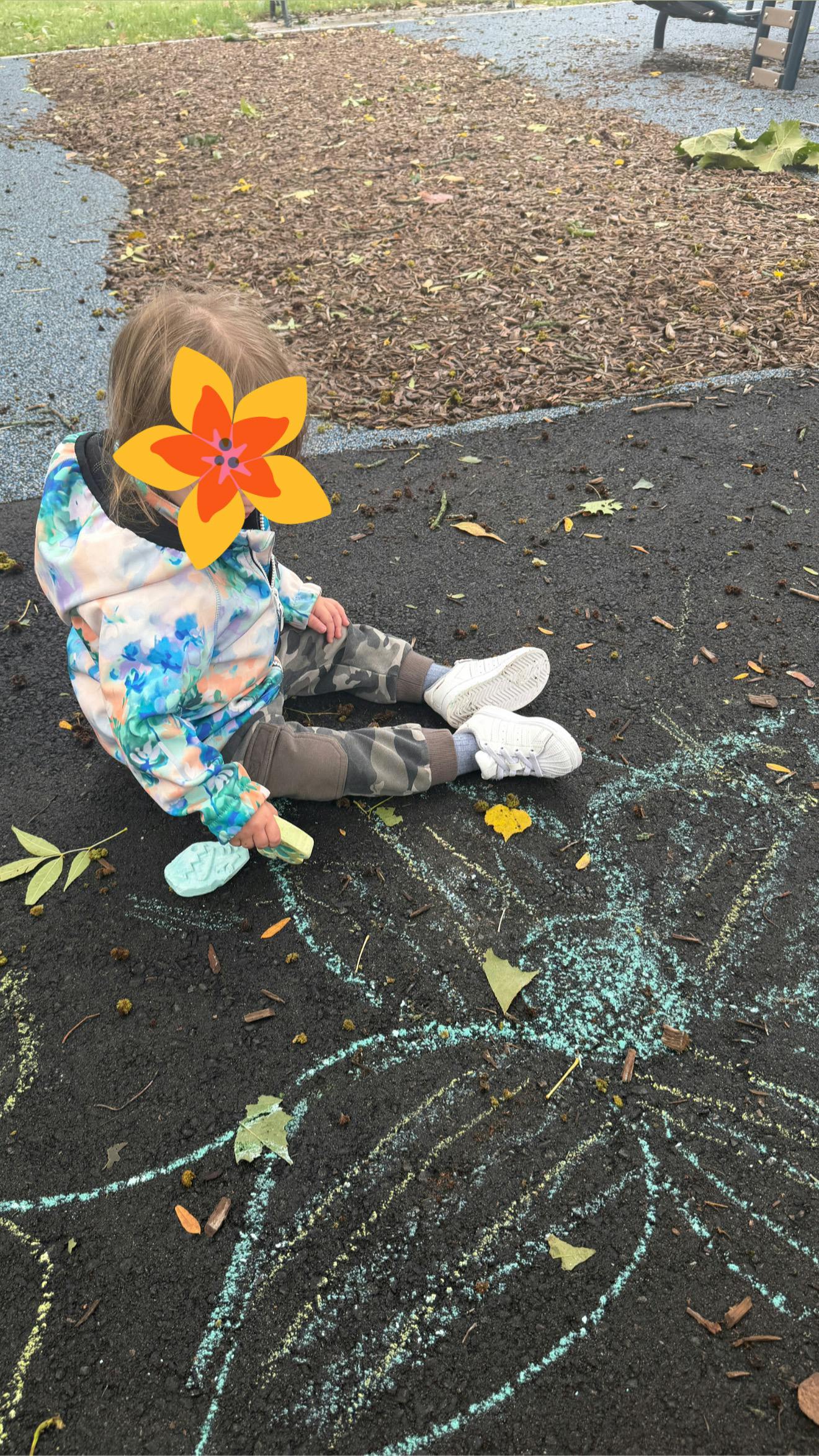Child sitting on playground pavement drawing with sidewalk chalk