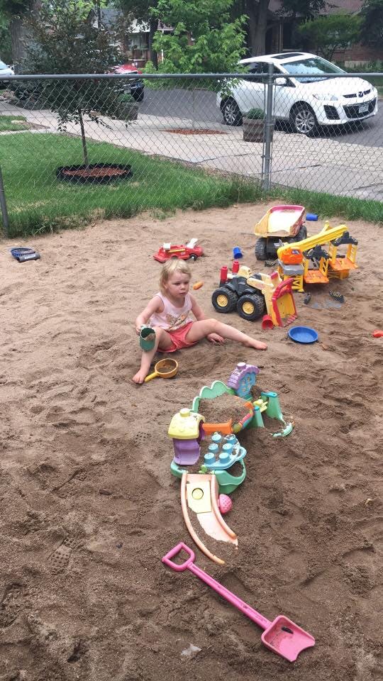 Child sitting in a sandbox with toys