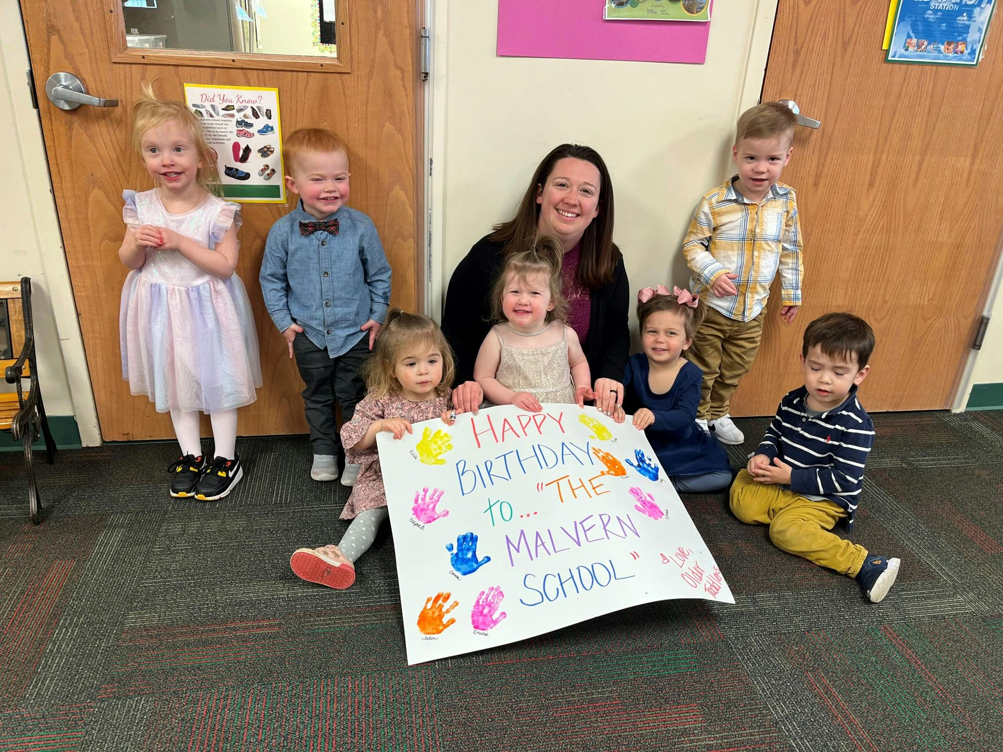 Adult and multiple children holding a sign that reads "Happy Birthday to The Malvern School"