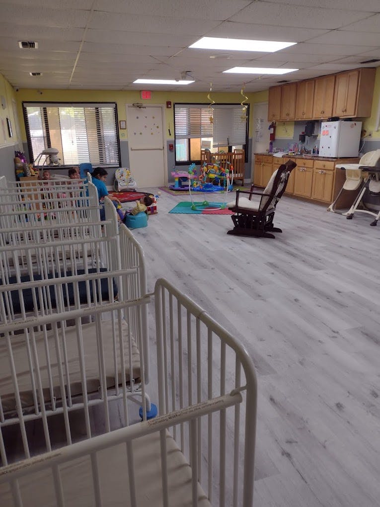 Daycare room with cribs, play area, and kitchen cabinets
