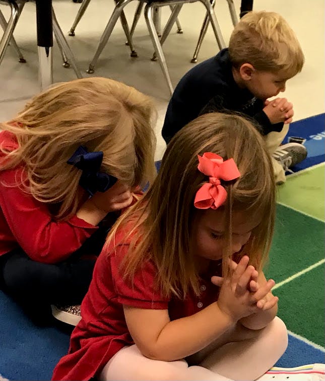 Three children sitting on the floor with hands clasped