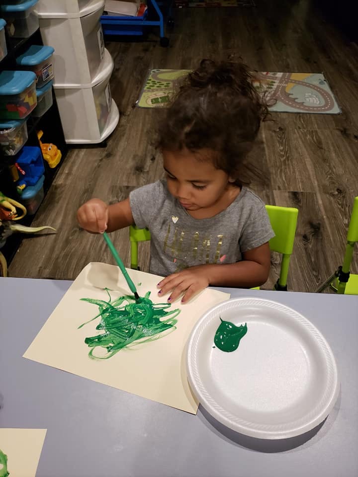 Child painting with green paint on paper