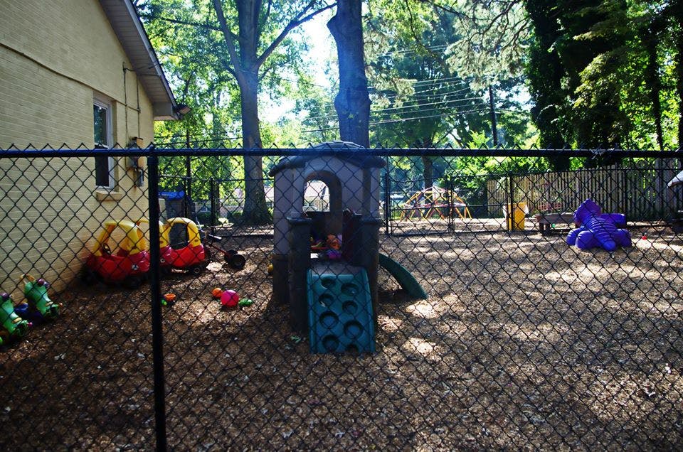 Outdoor playground with playhouse, slide, and toy cars behind a chain link fence