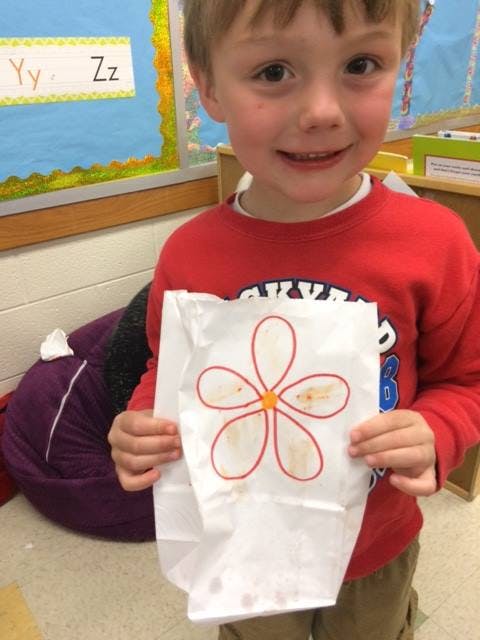Child holding a white paper bag with a red flower drawing