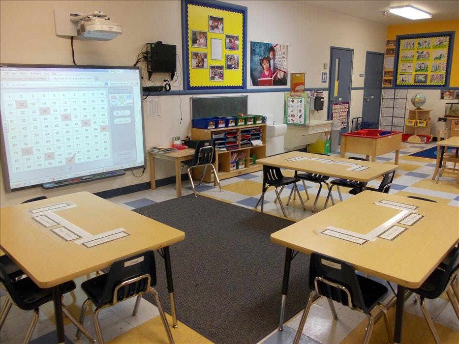 An empty classroom with desks, chairs, and an interactive whiteboard displaying numbers
