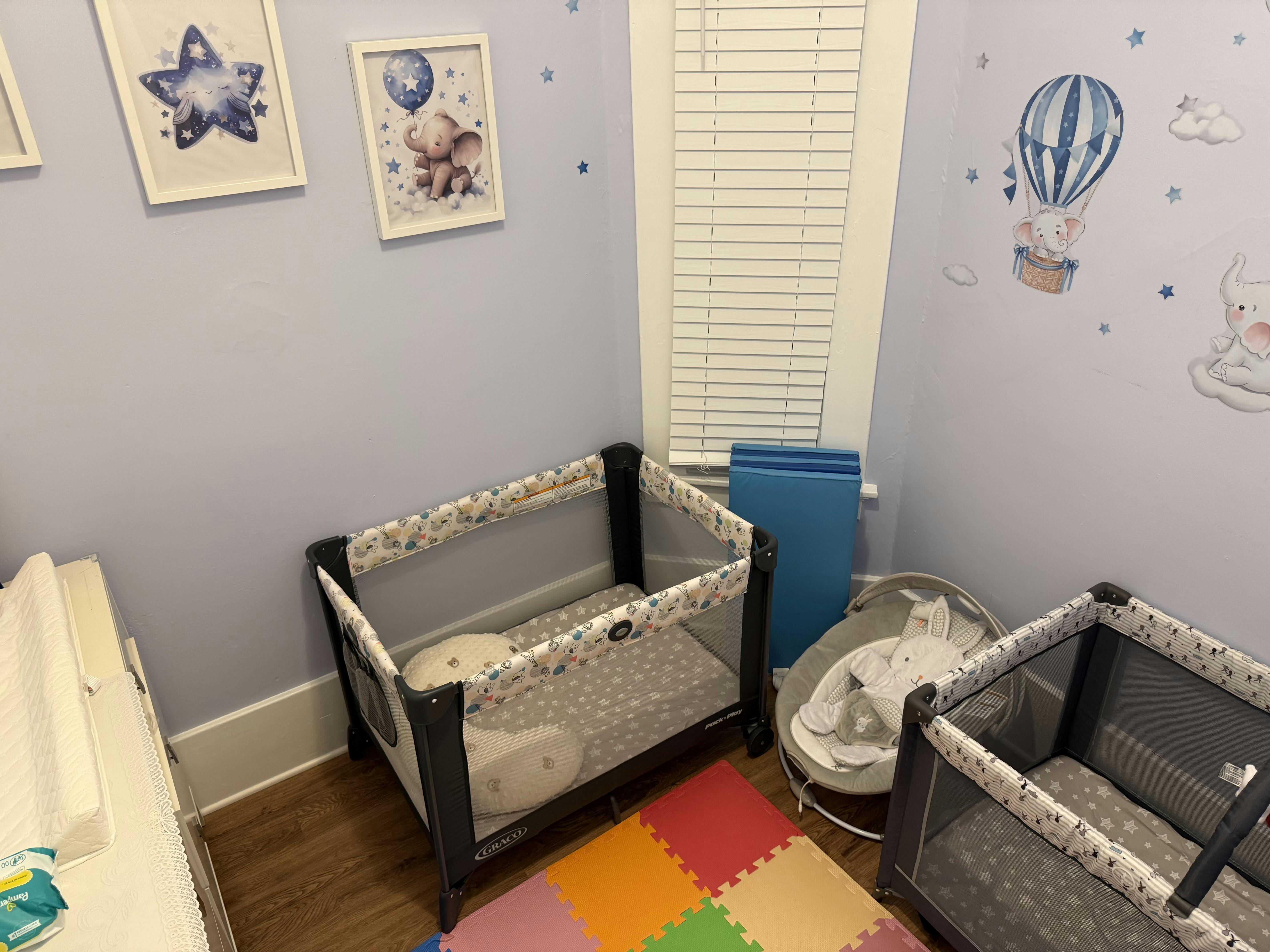 Two baby cribs and a baby bouncer in a room with wall decorations