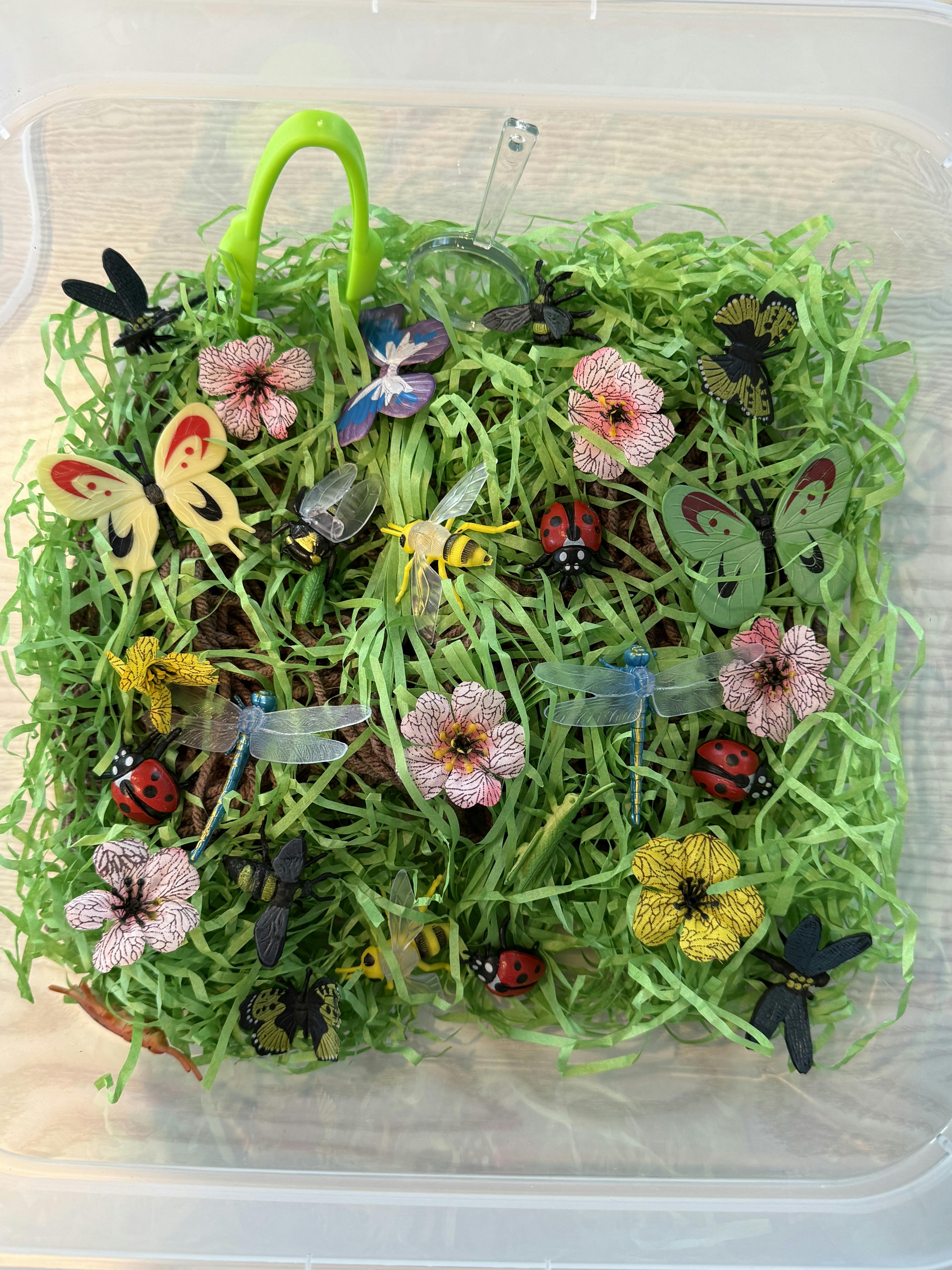 Plastic insect and flower toys inside a container with green paper grass