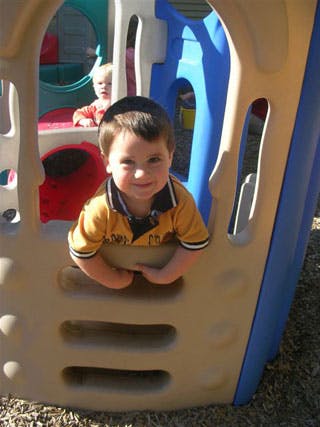 Child in a yellow shirt looking out from a play structure