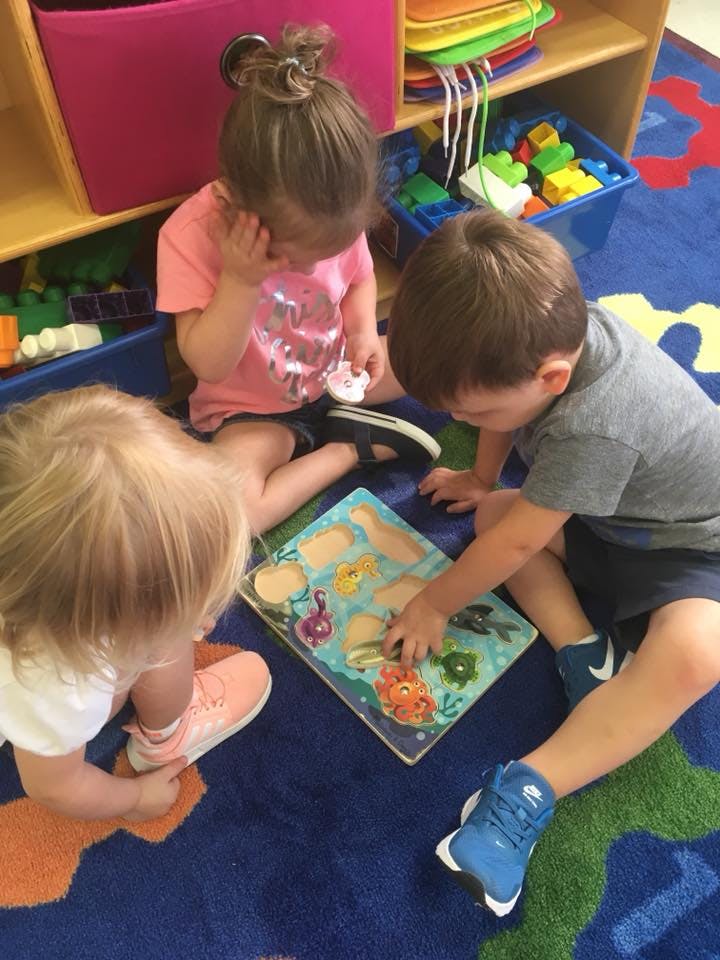 Three children playing with a puzzle on a colorful rug