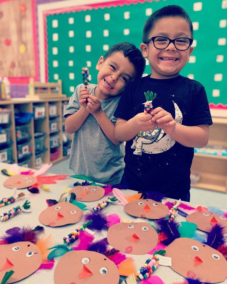 Two children holding small crafts in a classroom