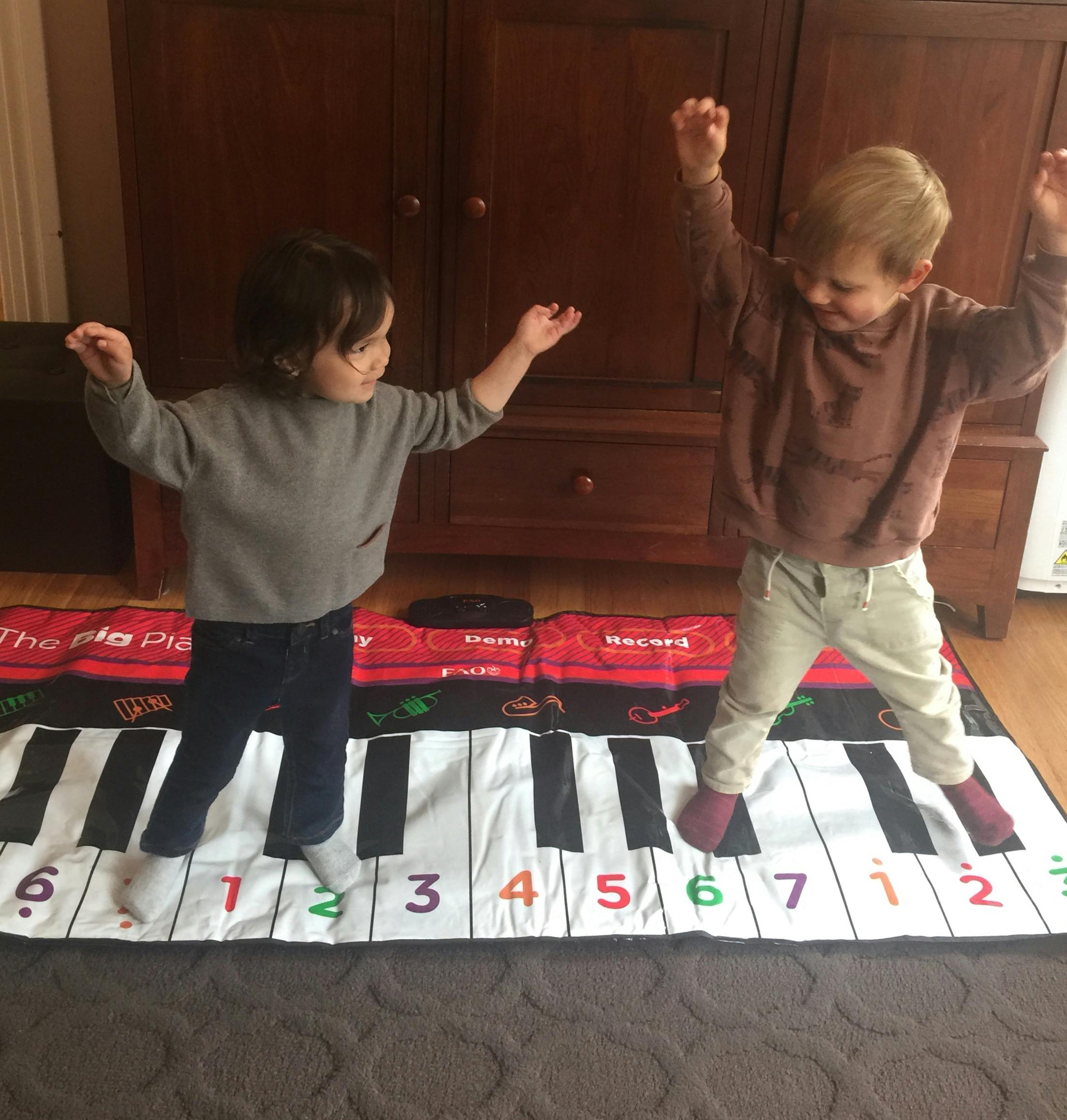 Two children playing on a floor piano mat