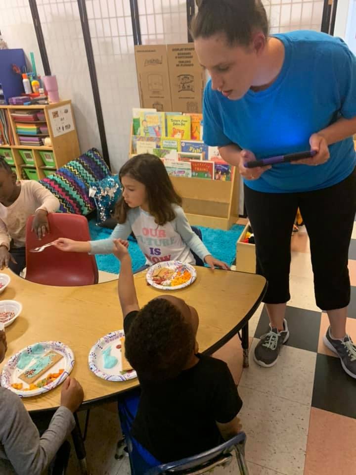 Adult holding a tablet watching children at a table with plates of food