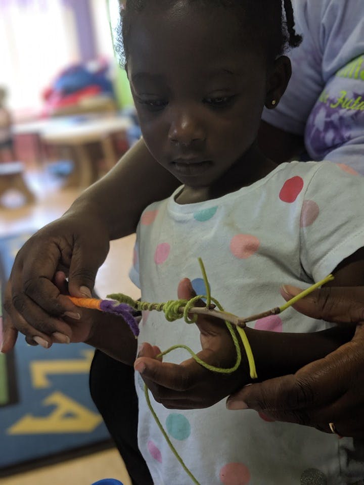 Child and adult hands working on a craft with string and a stick