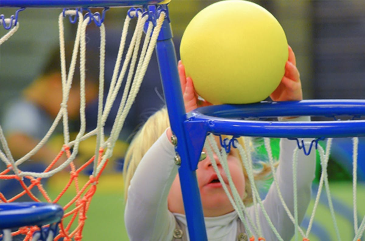 Child holding a yellow ball over a basketball hoop