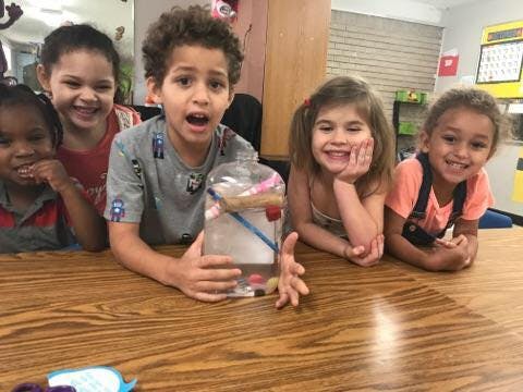 Children gathered around a table with a clear container