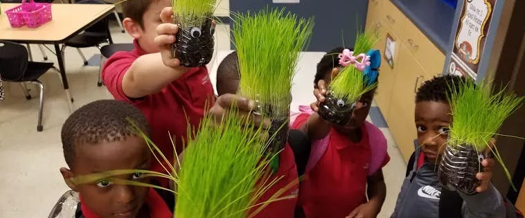 Children holding up crafts with green grass growing out of them
