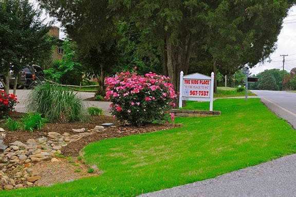 Sign for "The Kids Place" next to a bush with pink flowers
