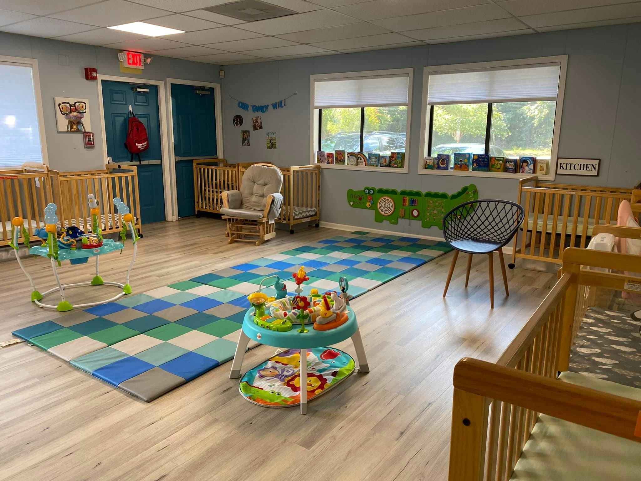 A colorful childcare room with cribs, play mats, and toys