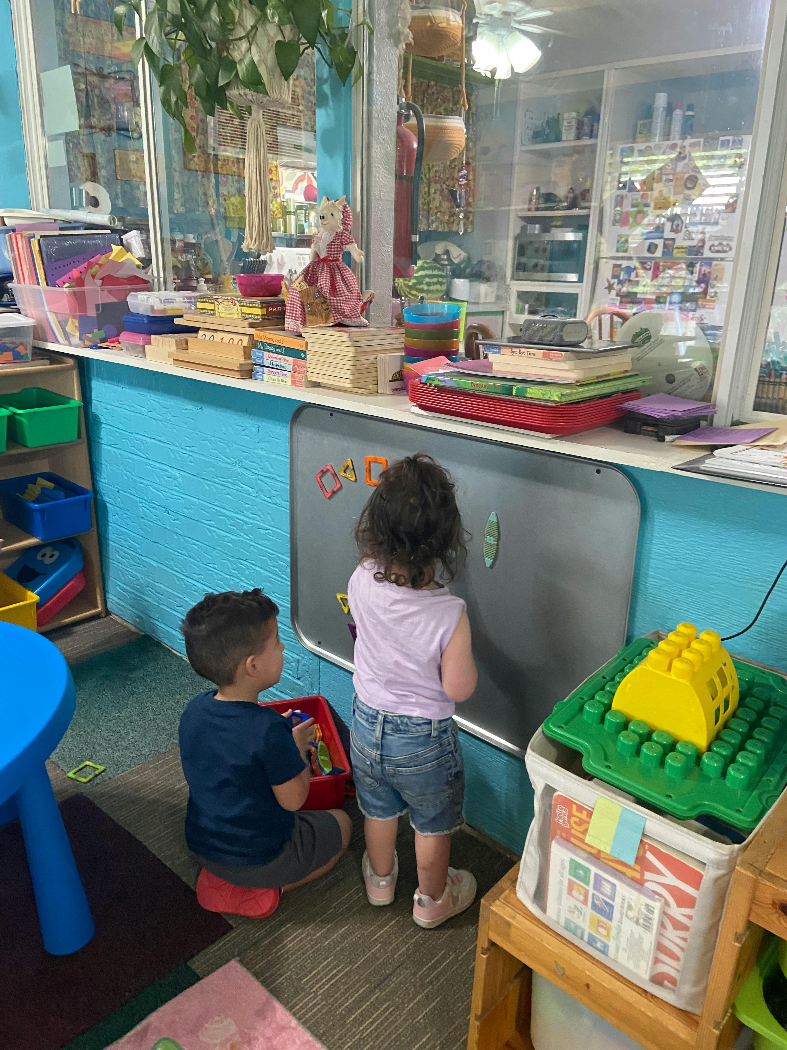 Two children playing with magnetic shapes on a wall board in a classroom