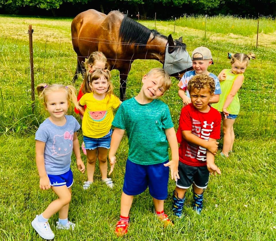 Group of children standing in a field with a horse