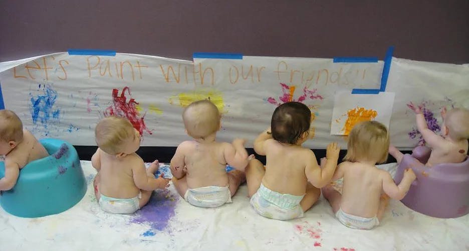 Multiple babies sitting and painting on a large sheet of paper