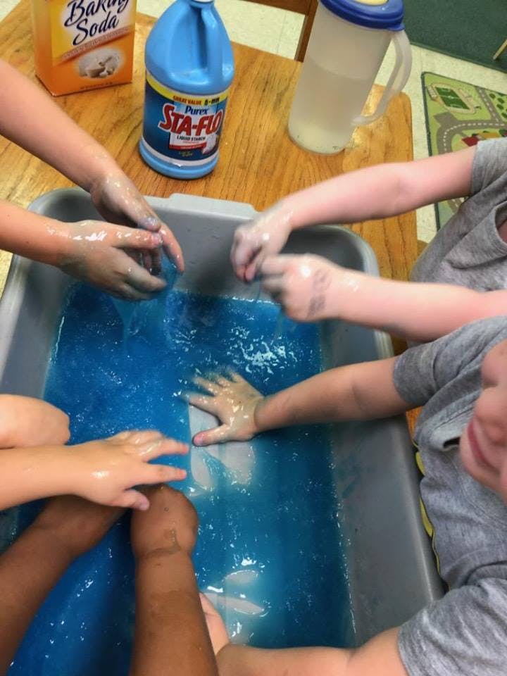 Multiple children's hands playing in a bin of blue liquid