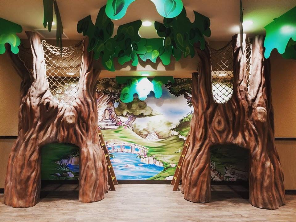 Indoor play area with two tree-like structures and a painted mural