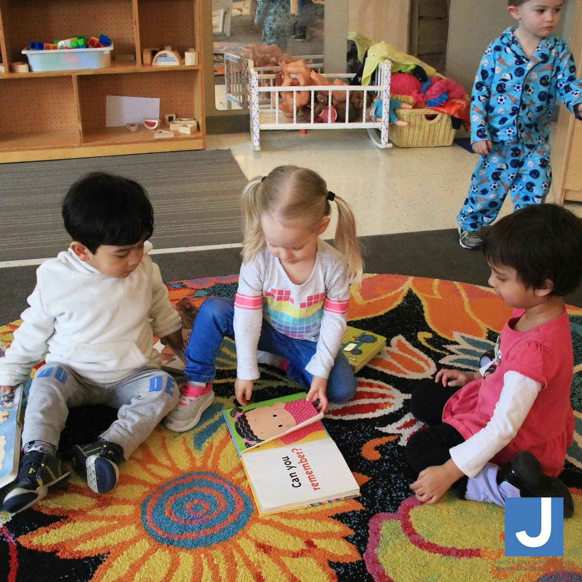 Three children sitting on a rug looking at books