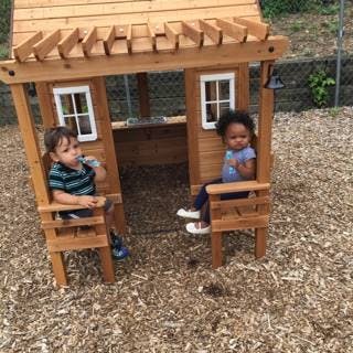 Two children sitting in a wooden playhouse