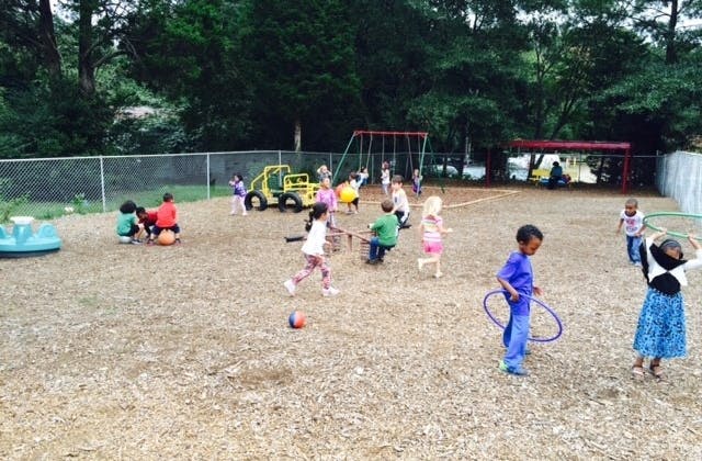 Children playing on a playground with wood chips, swings, and toys