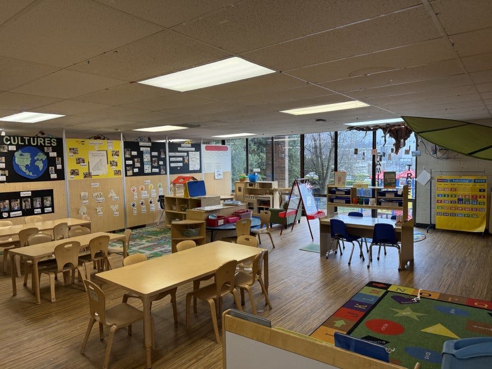 Empty preschool classroom with small tables, chairs, and learning decorations on walls