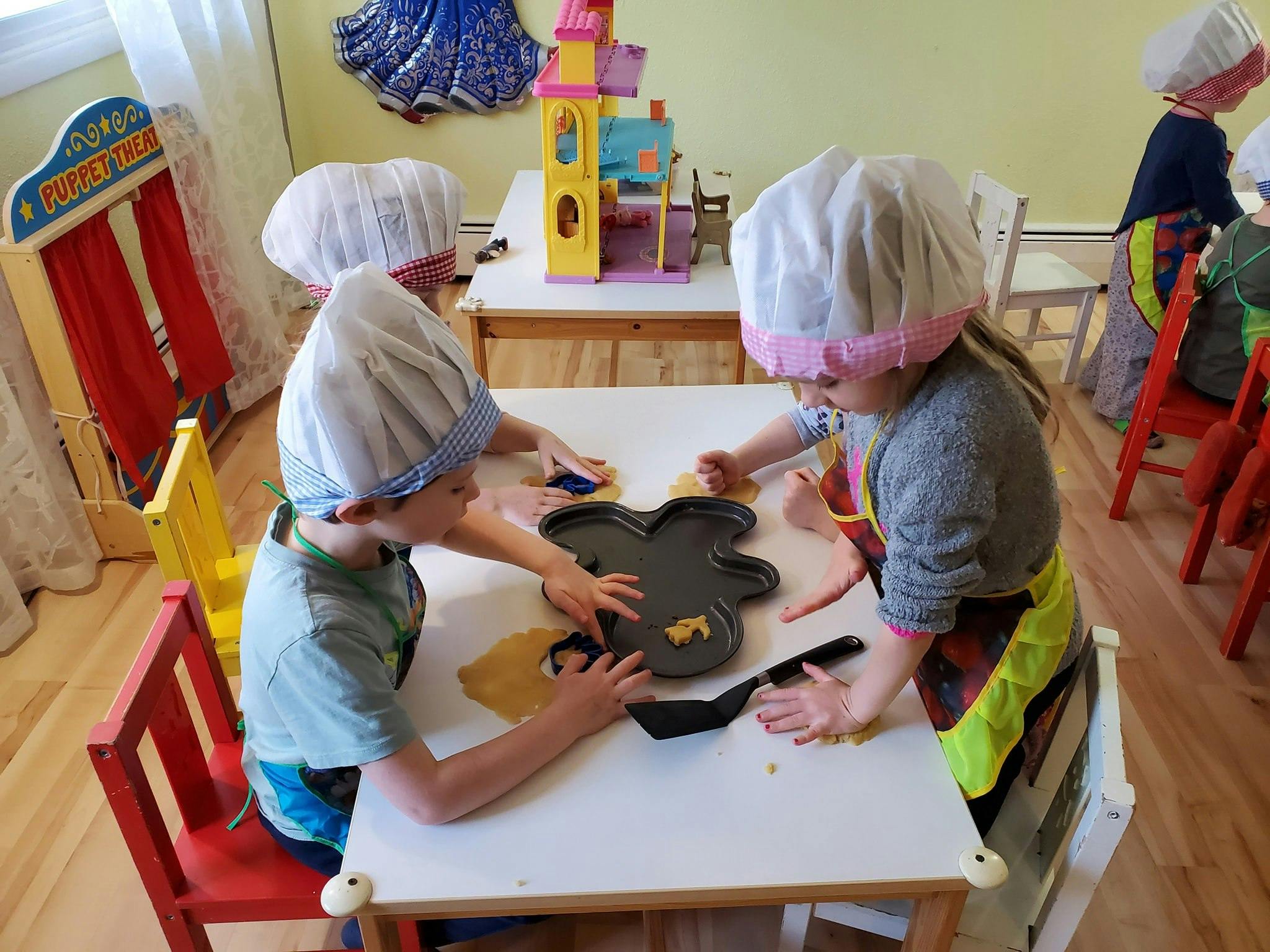 Children in chef hats and aprons playing with dough at a table