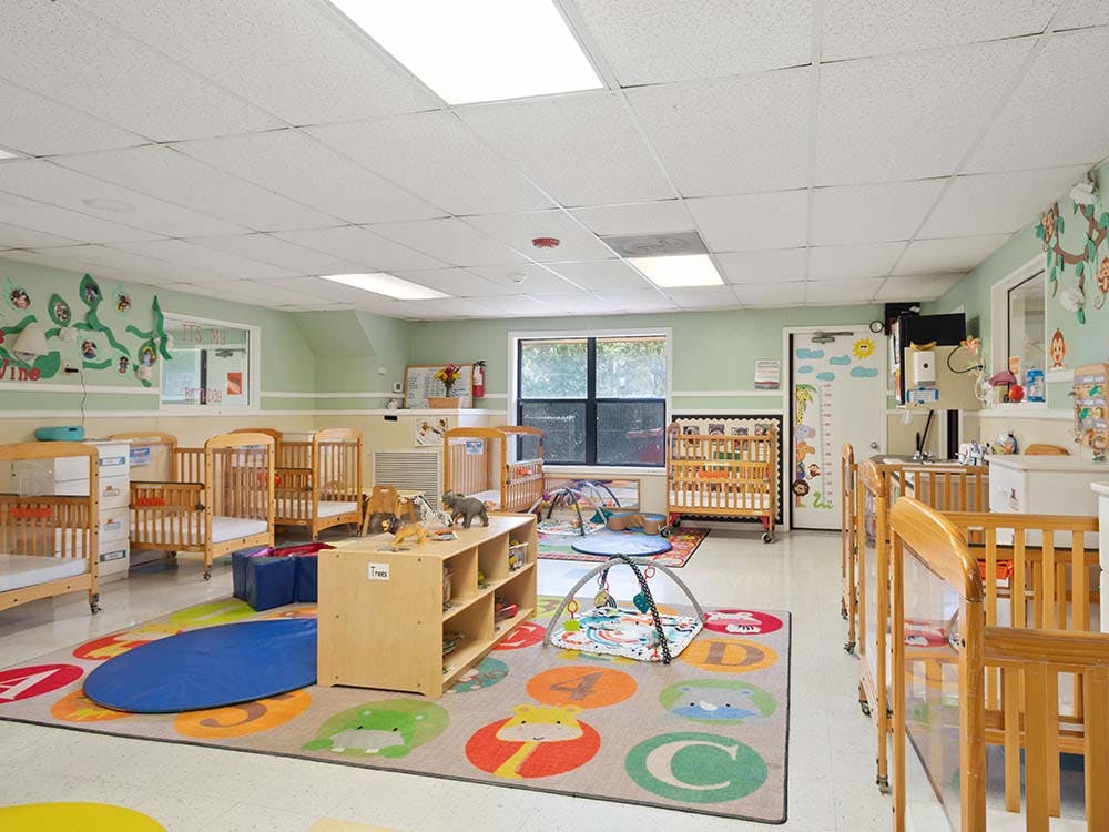 Classroom with multiple wooden cribs and a colorful alphabet rug