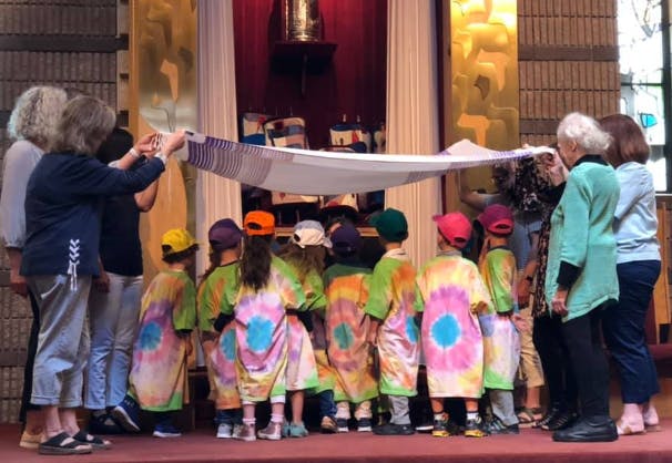 Adults holding a white cloth over a group of children