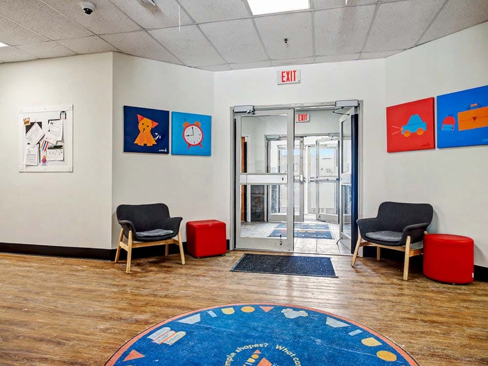Lounge area with chairs, ottomans, children's art on walls, and an exit door