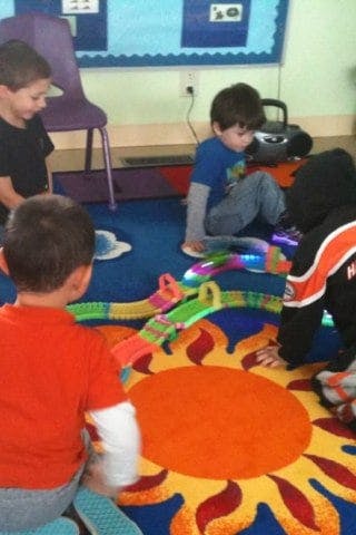 Children playing with a toy car track on a sun-patterned rug