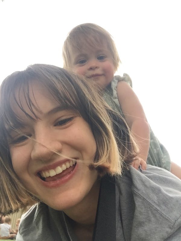 Person smiling at camera with a child on their shoulders
