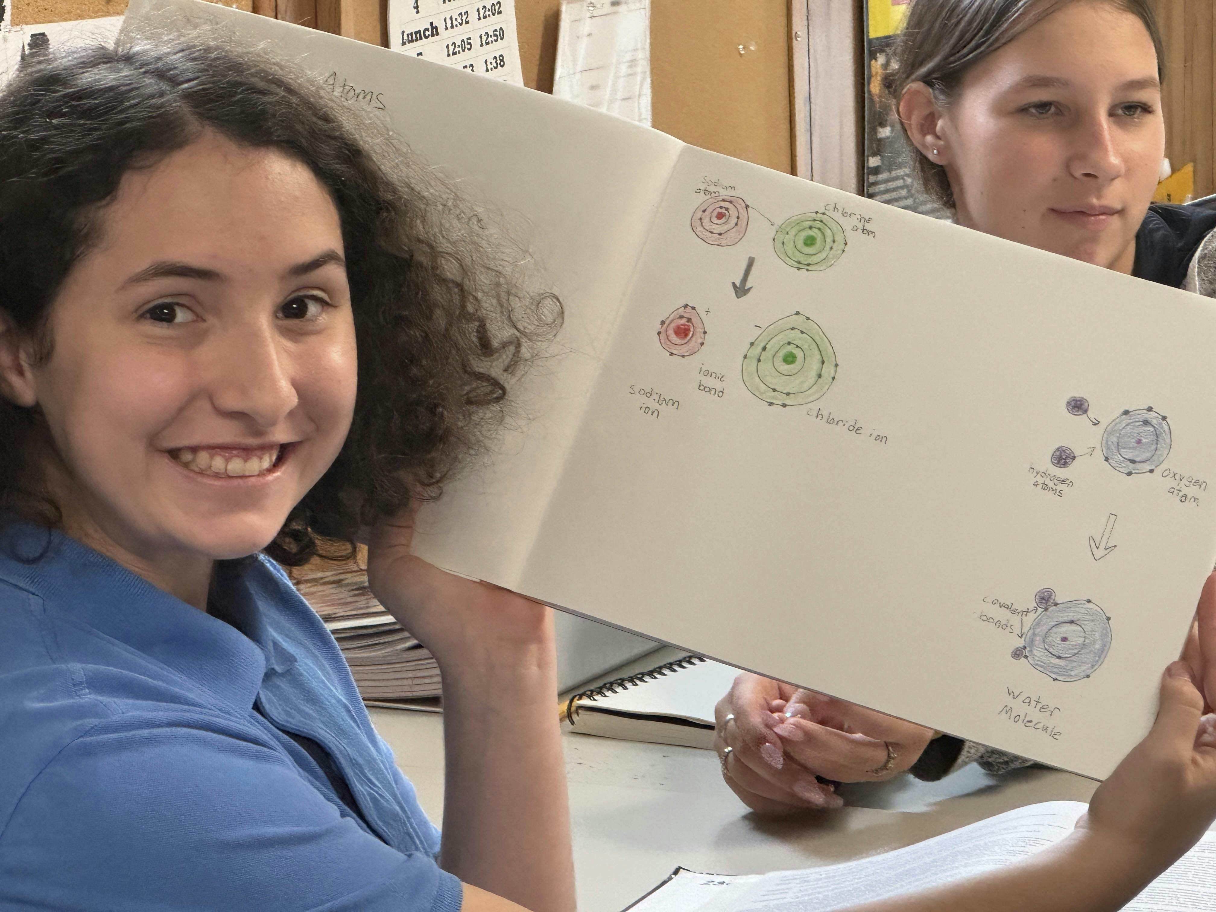 Smiling person holding a drawing of atoms, ions, and a water molecule