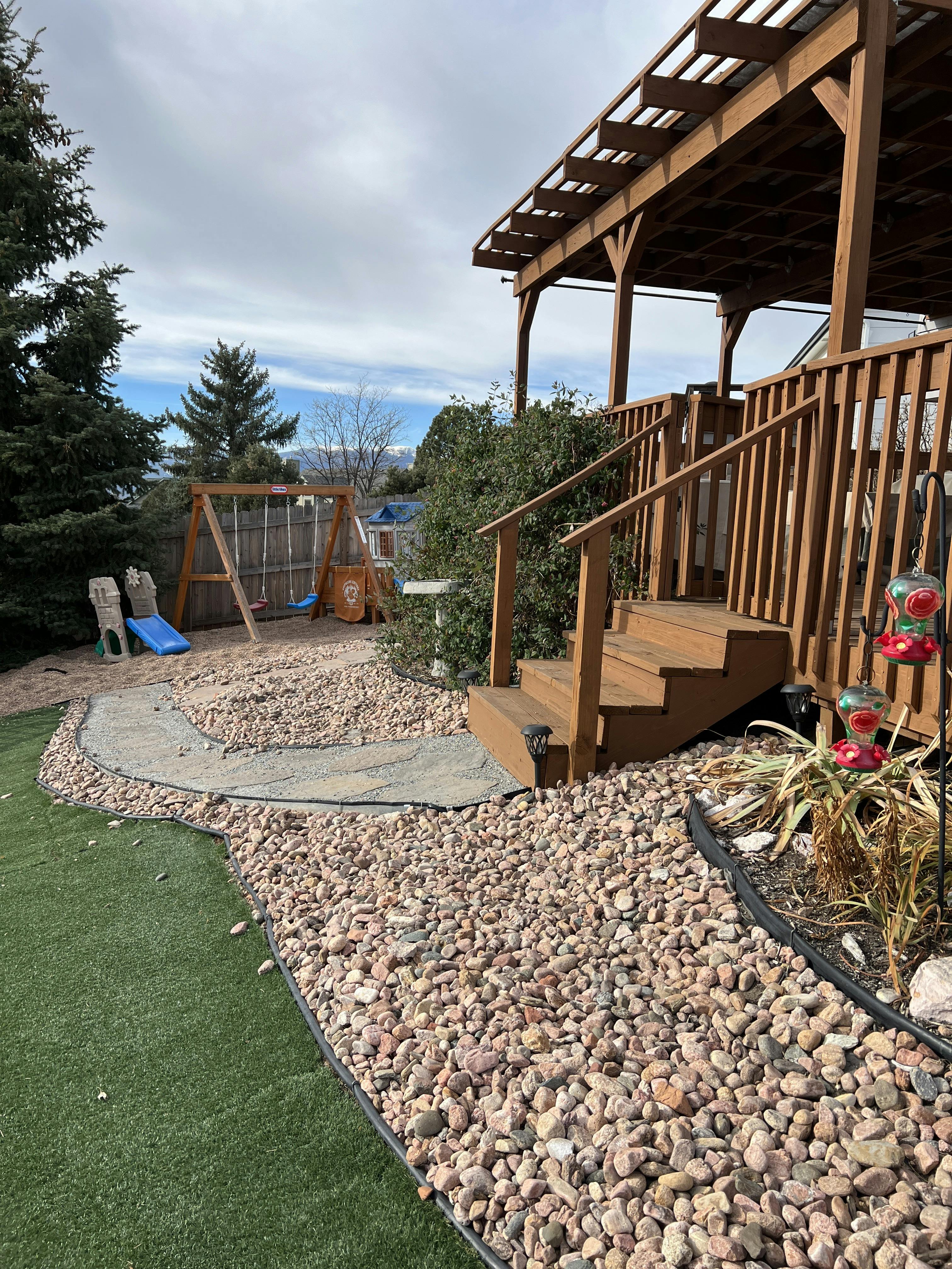 backyard with a wooden deck, swing set, and rock landscaping