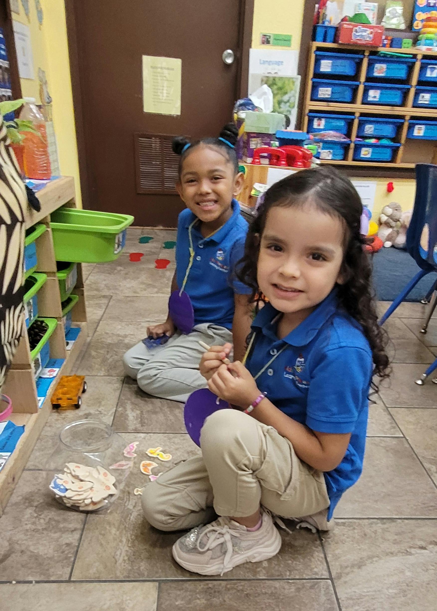 Two children sitting on a classroom floor playing with cutout shapes