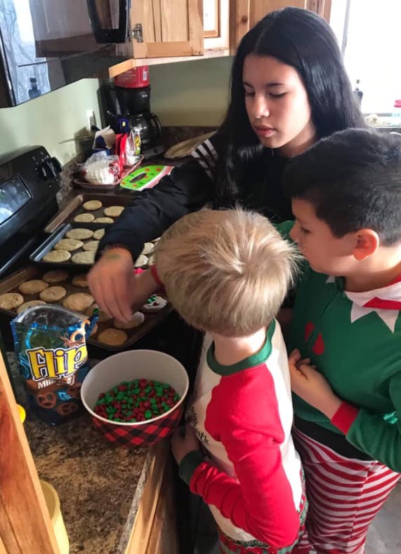 Teen and two children decorating cookies in a kitchen