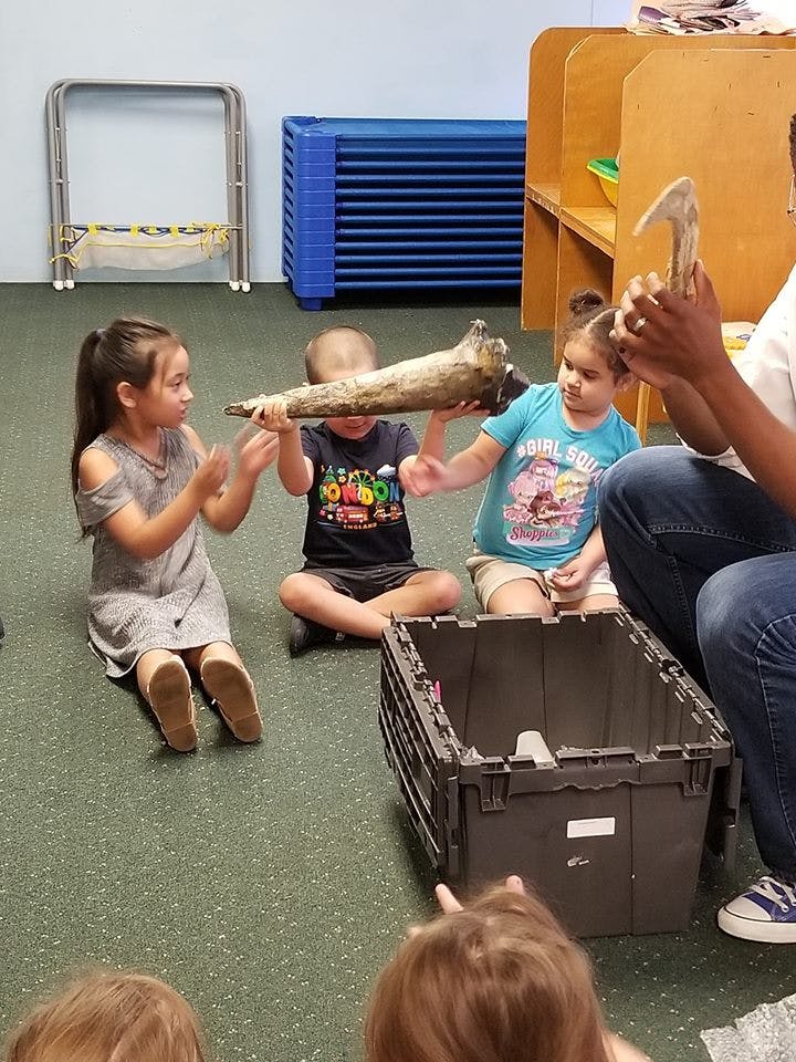 Three children and an adult holding objects in a classroom