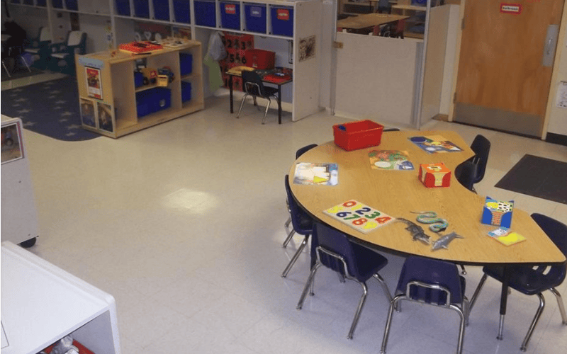 Classroom with a table and chairs in the foreground and shelves with toys