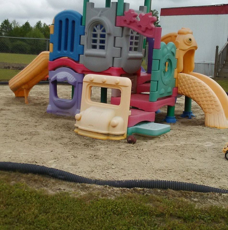 Colorful playground structure with slides and a bus-shaped entrance on a sandy surface