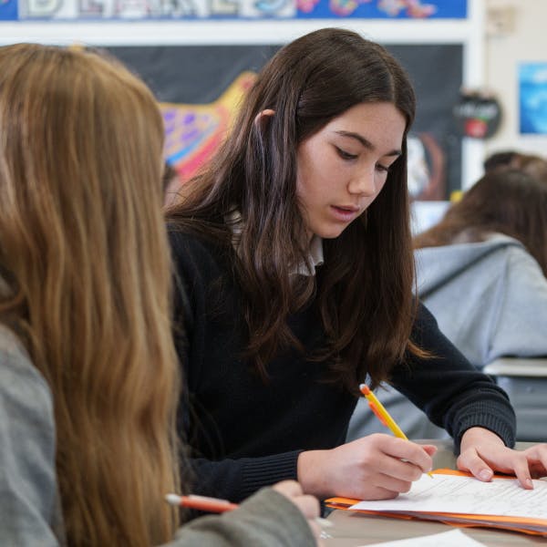 Teen writing on paper with a pencil in a classroom