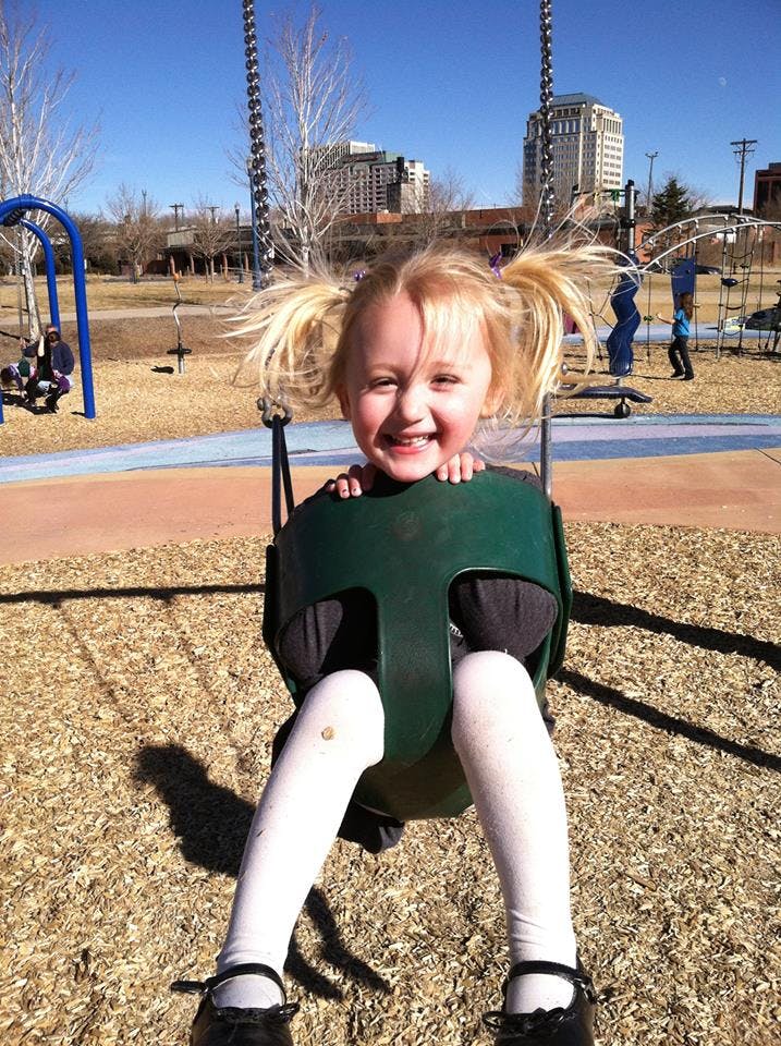 Child with pigtails in a swing at a playground