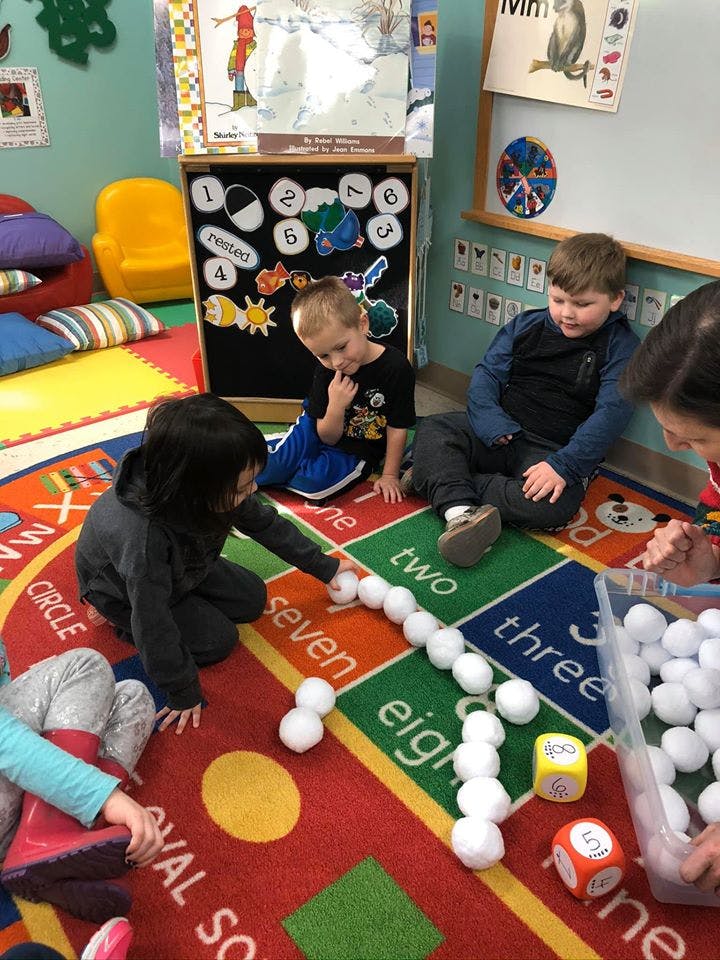 Children playing with white balls and dice on a colorful rug with numbers